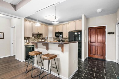 Kitchen with black appliances, a kitchen breakfast bar, decorative backsplash, hanging light fixtures, and cream cabinetry
