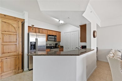 Kitchen featuring stainless steel appliances, dark stone counters, brown cabinetry, a peninsula, and light tile patterned flooring