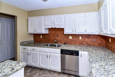Kitchen with dishwasher, tasteful backsplash, white cabinets, light stone countertops, and a textured ceiling