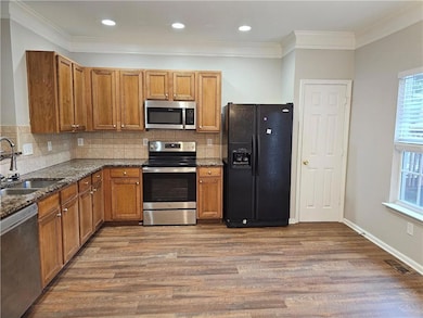 Kitchen featuring stainless steel appliances, a sink, brown cabinets, dark stone countertops, and ornamental molding