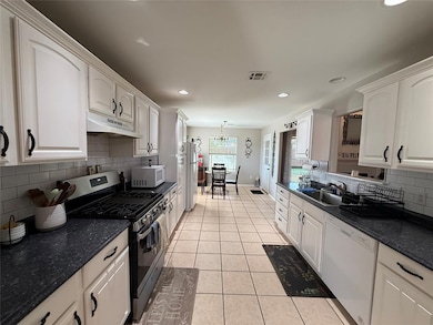 Kitchen with white appliances, under cabinet range hood, white cabinets, tasteful backsplash, and light tile patterned floors