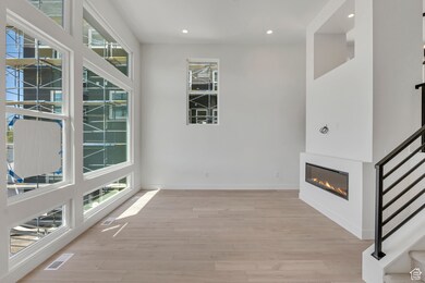 Interior space with a glass covered fireplace, recessed lighting, light wood finished floors, and stairway