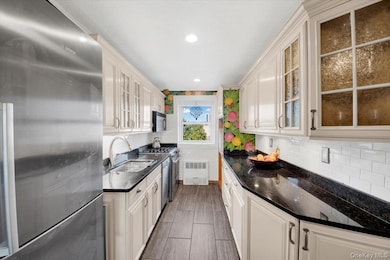 Kitchen featuring appliances with stainless steel finishes, glass insert cabinets, tasteful backsplash, dark stone countertops, and wood tiled floors