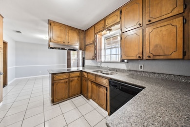 Kitchen with brown cabinets, black appliances, light tile patterned floors, and a peninsula