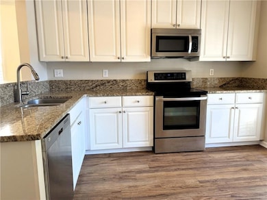 Kitchen featuring stainless steel appliances, dark stone counters, dark wood-style floors, and white cabinets