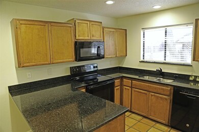 Kitchen featuring black appliances, a textured ceiling, a peninsula, brown cabinets, and light tile patterned flooring