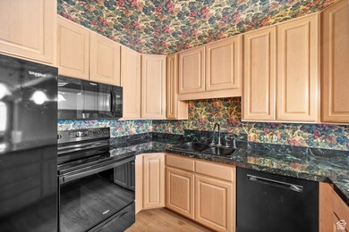Kitchen featuring black appliances, light brown cabinetry, tasteful backsplash, light wood-type flooring, and wallpapered walls