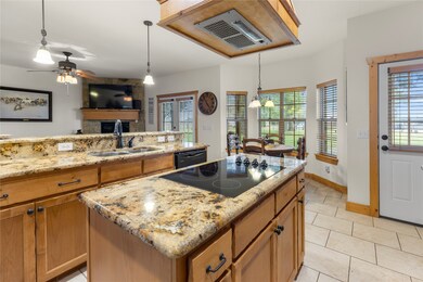 Kitchen featuring decorative light fixtures, brown cabinetry, a fireplace, and light stone counters