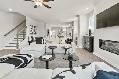 Living room featuring light wood-style flooring, recessed lighting, stairway, a glass covered fireplace, and a ceiling fan