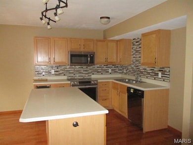 Kitchen with light brown cabinets, dark wood-type flooring, stainless steel appliances, light countertops, and a kitchen island