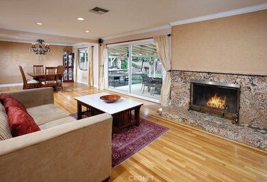 The living room is bathed in natural light from a multitude of windows and is enhanced by modern recessed lighting, crown molding, a custom raised hearth fireplace with granite surround, easy access to the backyard through the sliding glass doors and