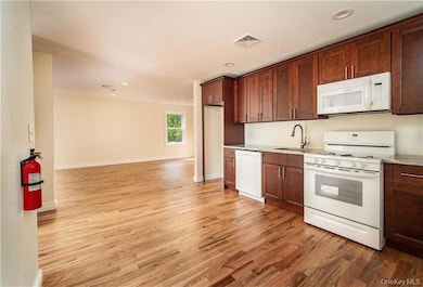 Kitchen featuring white appliances, light wood-style flooring, light countertops, recessed lighting, and open floor plan