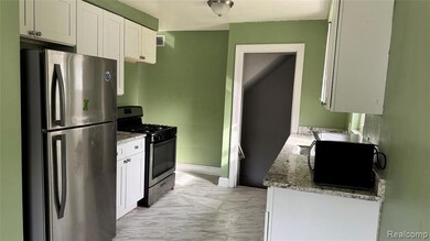 Kitchen featuring appliances with stainless steel finishes, white cabinets, light marble finish flooring, and light stone counters