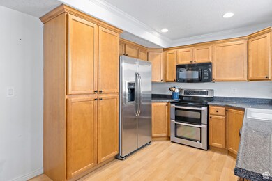Kitchen with stainless steel appliances, light wood-type flooring, crown molding, dark countertops, and recessed lighting