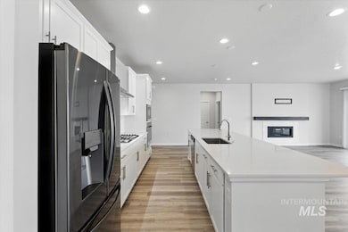 Kitchen with appliances with stainless steel finishes, recessed lighting, white cabinets, light wood-type flooring, and a spacious island
