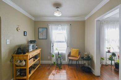 Living area with a textured wall, ornamental molding, hardwood / wood-style flooring, and baseboards