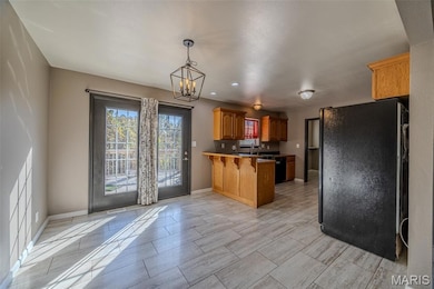 Kitchen featuring freestanding refrigerator, a peninsula, a kitchen bar, hanging light fixtures, and brown cabinetry