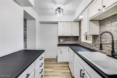 Kitchen with a textured ceiling, white cabinets, dark countertops, light wood finished floors, and backsplash