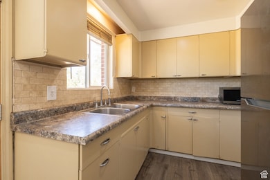 Kitchen featuring cream cabinets, dark wood-style flooring, stainless steel microwave, and backsplash