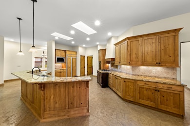 Kitchen featuring brown cabinets, light stone counters, backsplash, a skylight, and recessed lighting