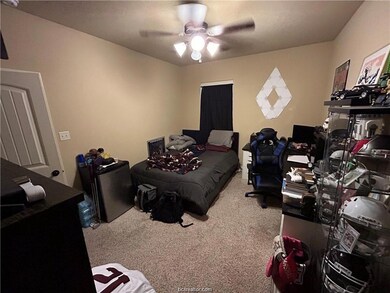 Bedroom featuring light colored carpet, an office area, ceiling fan, and refrigerator