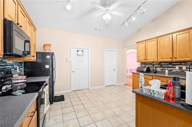 Kitchen with track lighting, range with electric stovetop, black microwave, tasteful backsplash, and vaulted ceiling