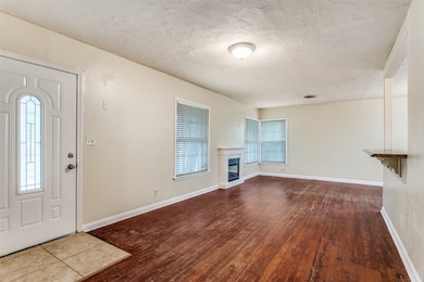 Unfurnished living room with dark wood-type flooring, a glass covered fireplace, and a textured ceiling