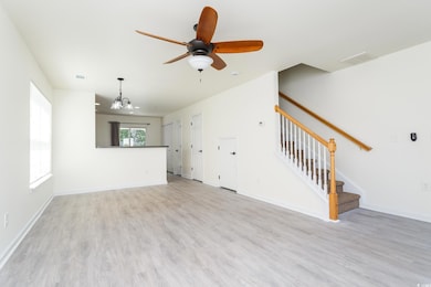 Unfurnished living room with stairs, light wood finished floors, a chandelier, and a ceiling fan