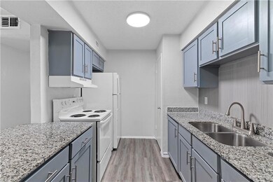 Kitchen featuring light hardwood / wood-style floors, a textured ceiling, light stone counters, white electric stove, and sink
