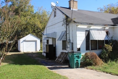 View of home's exterior featuring a chimney, a detached garage, a lawn, driveway, and an outdoor structure