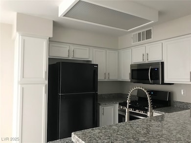 Kitchen featuring appliances with stainless steel finishes, white cabinetry, and light stone countertops