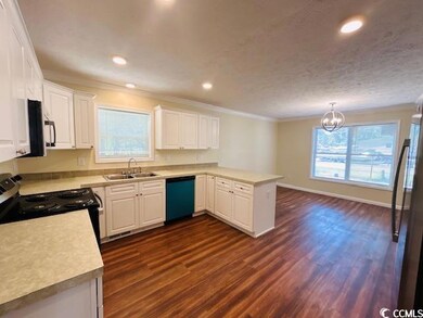 Kitchen with black appliances, a sink, dark wood finished floors, a peninsula, and crown molding