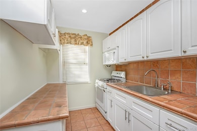 Kitchen featuring tile countertops, white appliances, light tile patterned flooring, white cabinets, and tasteful backsplash