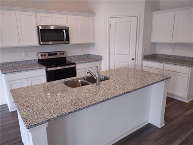 Kitchen with stainless steel appliances, dark wood finished floors, white cabinets, and light stone countertops