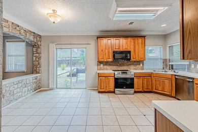Kitchen featuring a textured ceiling, ornamental molding, backsplash, brown cabinetry, and appliances with stainless steel finishes