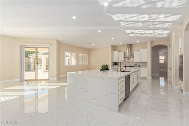 Kitchen with arched walkways, light marble finish flooring, light stone counters, white cabinetry, and recessed lighting