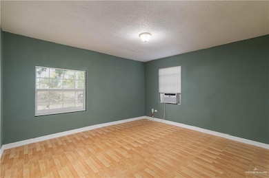 Unfurnished room featuring cooling unit, light wood-style floors, baseboards, and a textured ceiling