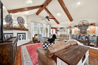 Living area featuring beam ceiling, high vaulted ceiling, dark wood-style flooring, a fireplace with raised hearth, and ceiling fan