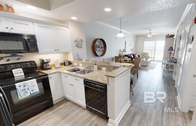 Kitchen with black appliances, a peninsula, white cabinets, crown molding, and light stone countertops