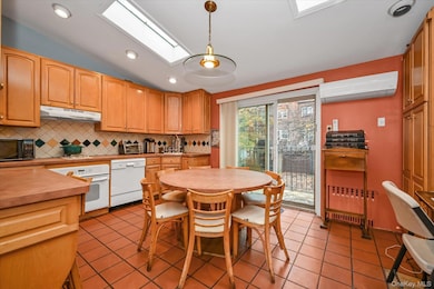 Kitchen with vaulted ceiling, light tile patterned floors, a skylight, tasteful backsplash, and white appliances