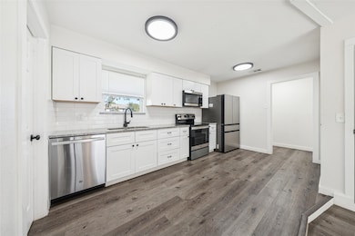 Kitchen with white cabinetry, stainless steel appliances, decorative backsplash, dark wood finished floors, and light stone countertops
