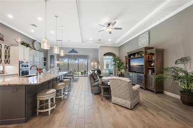 Living area featuring a tray ceiling, ceiling fan, light wood finished floors, ornamental molding, and recessed lighting