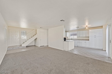 Unfurnished living room with light tile patterned floors, light carpet, and stairway