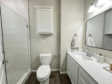 Bathroom featuring toilet, vanity, hardwood / wood-style floors, and tiled shower