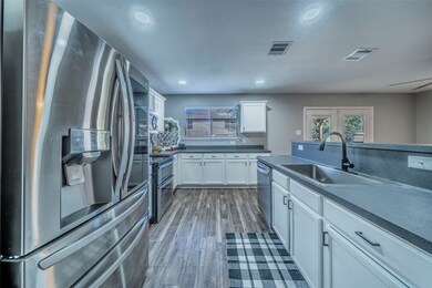 Kitchen featuring appliances with stainless steel finishes, dark countertops, dark wood-style floors, white cabinetry, and recessed lighting