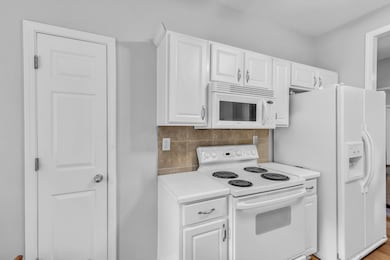 Kitchen with white appliances, light countertops, white cabinets, and backsplash
