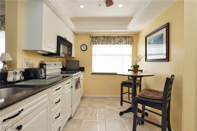 Kitchen featuring white electric stove, a raised ceiling, black microwave, a ceiling fan, and white cabinetry