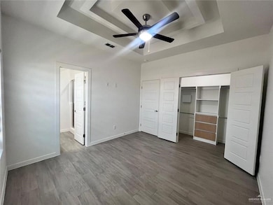 Unfurnished bedroom featuring a tray ceiling, a closet, baseboards, visible vents, and dark wood-style flooring