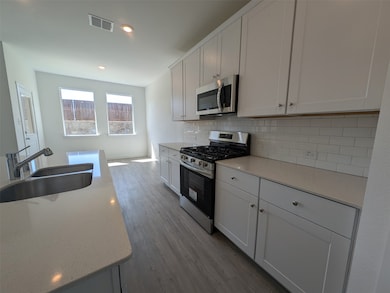 Kitchen with stainless steel appliances, backsplash, white cabinets, dark wood-style flooring, and light stone countertops