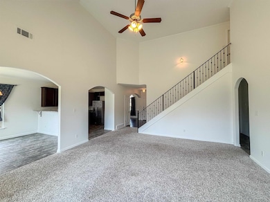 Unfurnished living room featuring arched walkways, carpet flooring, a towering ceiling, a ceiling fan, and stairs